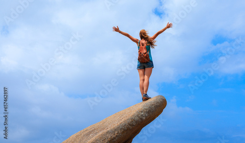 Woman with open arms standing on rock cliff enjoying fresh air- adventure, freedom, achievement concept