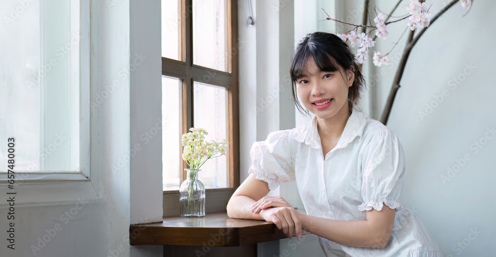 Portrait of a cute young woman smiling happily sitting at a table by the window.