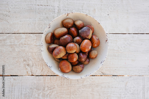 Close up chestnuts in a bowl on a wooden table with space for text. View from above.
 photo