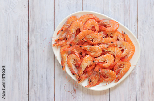 Boiled shrimp in a white plate on a light wooden background. Fresh shrimp, top view. Seafood. Healthy eating concept. Template for menu