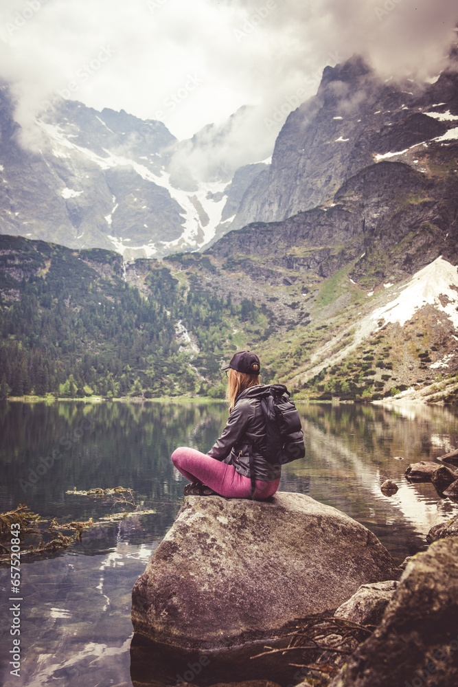 Relaxing in the mountains. A woman sitting on a stone by a mountain lake.