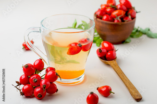 Cup with rosehip drink, bowl with rosehip berries, rosehip branches, berries in a wooden spoon on a light background, horizontal.