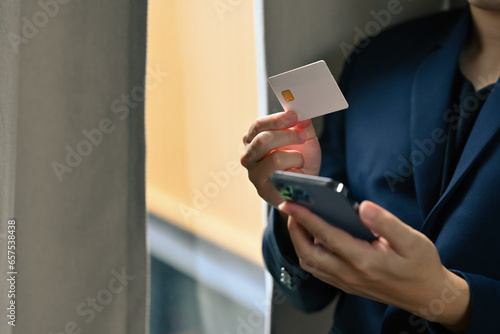 Male worker holding credit card, making transaction, paying bills, invoice on smartphone