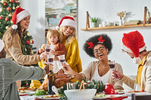 big multiethnic joyful family clinking their glasses at festive table wearing Santa hats, Christmas