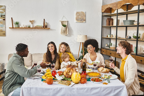 joyful multiethnic friends and family sharing tasty dinner while celebrating Thanksgiving together photo