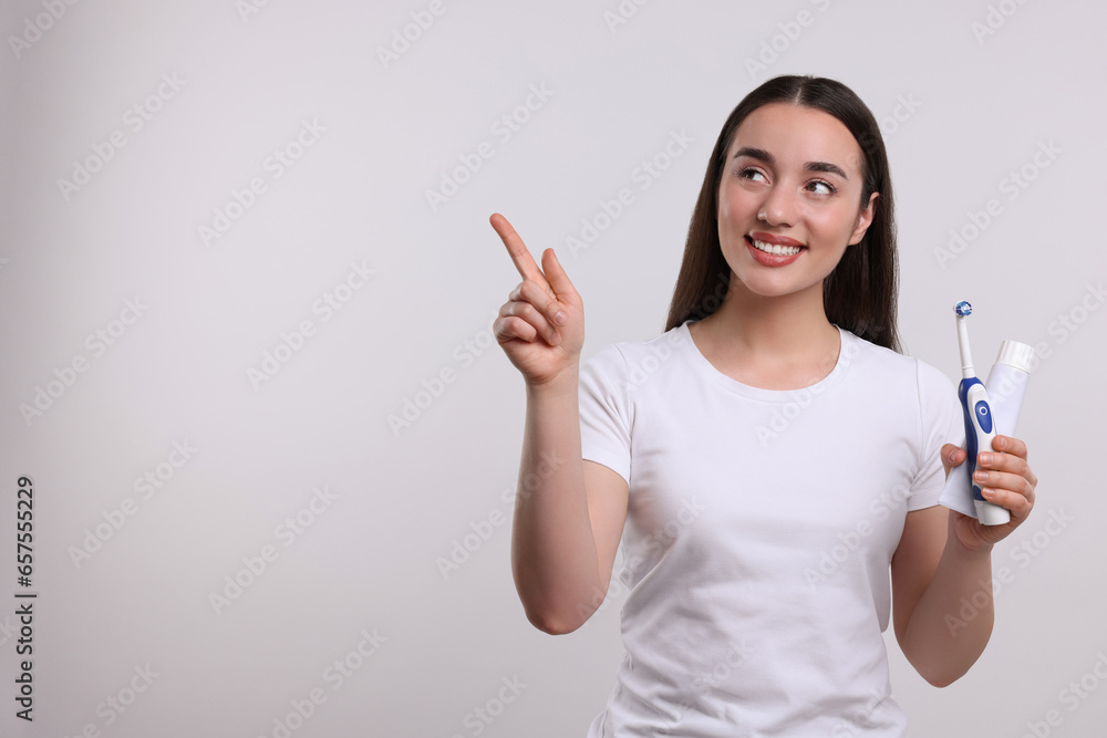 Happy woman with electric toothbrush and tube of toothpaste pointing on white background, space for text Happy woman with electric toothbrush and tube of toothpaste pointing on white background, space for text