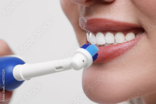 Woman brushing her teeth with electric toothbrush on white background  closeup