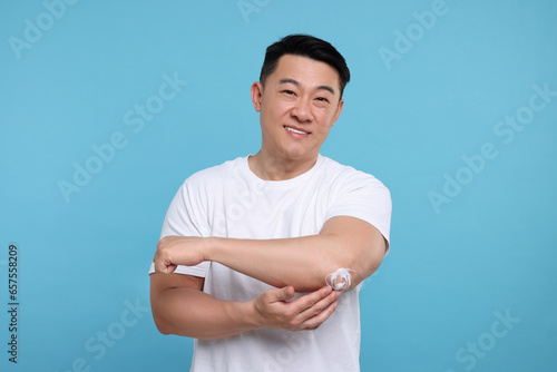 Photography Handsome man applying body cream onto his elbow on light blue background