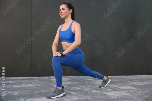Beautiful woman in stylish sportswear doing exercises near black wall outdoors