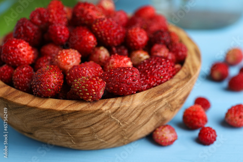 Fresh wild strawberries in bowl on light blue table, closeup
