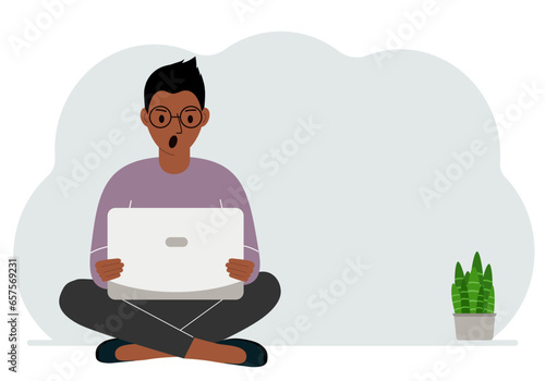A man sits cross-legged in his hands holding a laptop. The concept of work, education, reading, watching videos.
