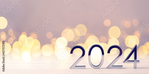 Metal numbers 2024 on a white table with Christmas trees and bokeh lights. Happy New Year 2024 is coming concept. photo