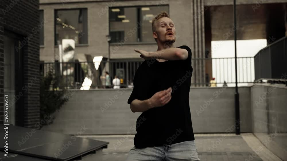 A man dances in front of houses. Black t-shirt, blonde. Slow motion. A man dances in front of houses. Black t-shirt, blonde. Slow motion.