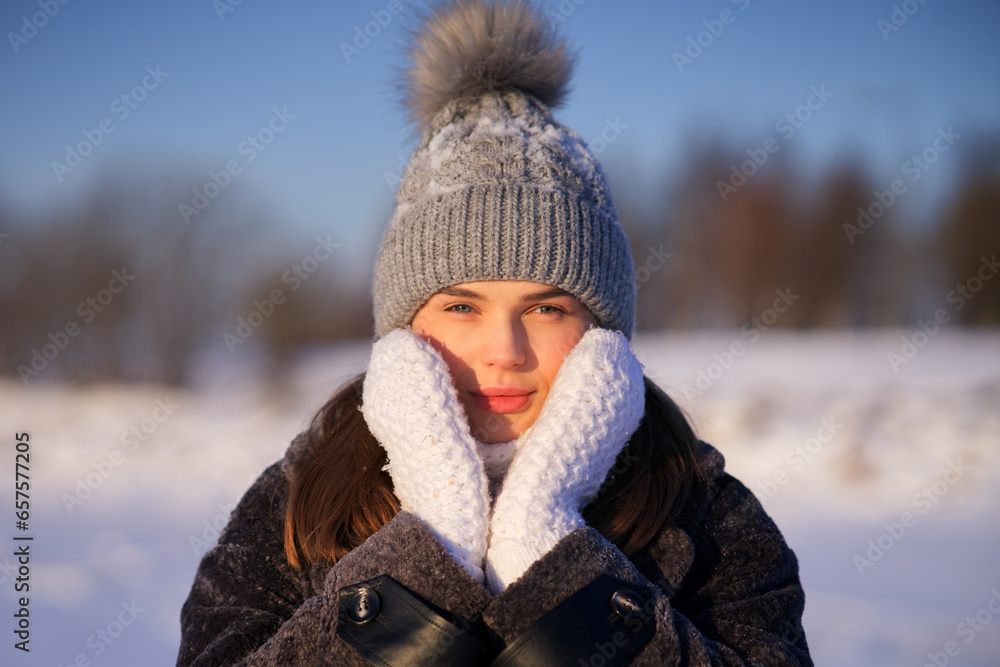 Portrait of beautiful girl young frozen pretty woman standing walking in winter snowy park at cold snow frosty day in hat, scarf, in gloves looking at camera Portrait of beautiful girl young frozen pretty woman standing walking in winter snowy park at cold snow frosty day in hat, scarf, in gloves looking at camera