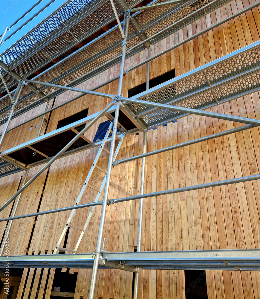 Scaffolding made of galvanized pipes is installed around  building, where facades made of boards and the insulation of the suspended structure are being assembled. larch paneling with cottage wood