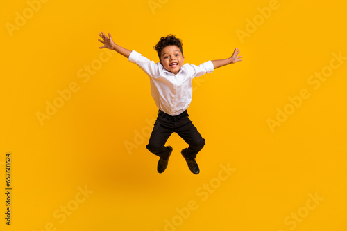 Full size photo of optimistic active schoolboy with curly hair dressed white shirt jumping having fun isolated on yellow color background