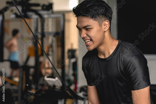 A young handsome asian man grunts while doing tricep pushdowns at the gym. photo