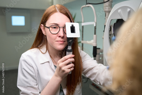 Red-haired ophthalmologist checks the eyes of a patient