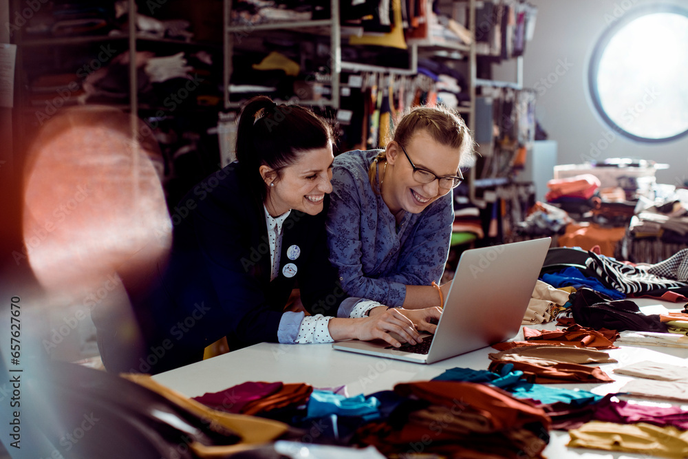 Two young female colleagues using the laptop while working in a textile manufacturing company Two young female colleagues using the laptop while working in a textile manufacturing company