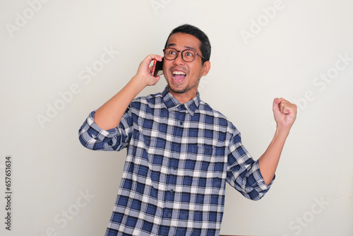 Adult Asian man showing cheerful expression when answering a phone call photo