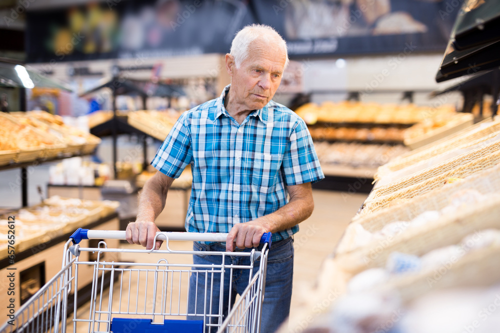 Mature senor choosing bread and baking in grocery section of supermarket