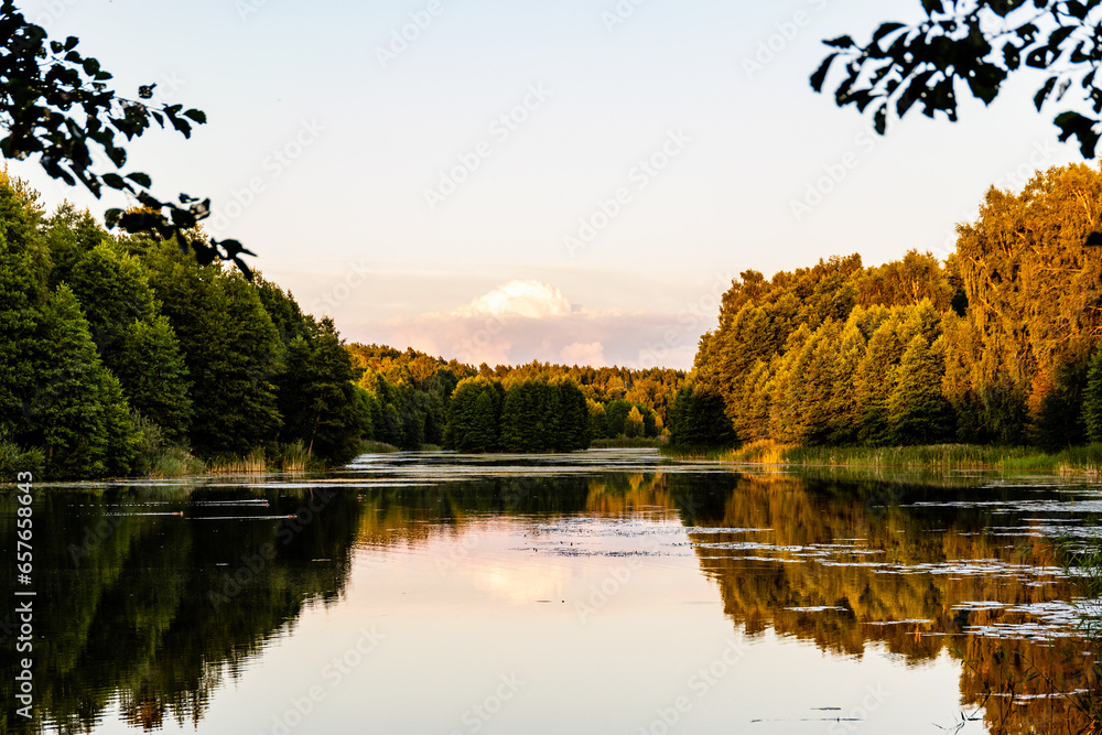 Summer evening at the lakeside of Latvia. Lake in summer during sunset. Nordic summer night at river.  Sunset over the lake. Sun is setting and reflecting trees in evening water. Idyllic evening photo