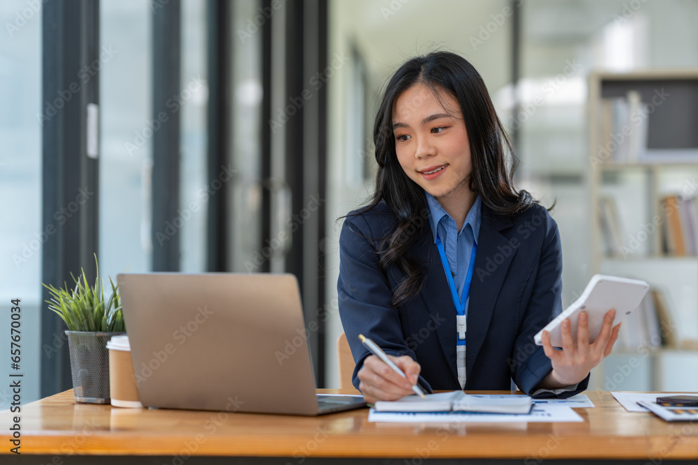 Asian businesswoman smiling at the idea of working at a calculator to calculate income. on the laptop at the office. Asian businesswoman smiling at the idea of working at a calculator to calculate income. on the laptop at the office.