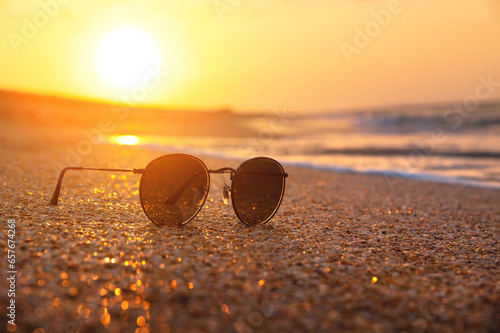 Stylish round sunglasses lie on the wet sand of the sea beach in the rays of the setting sun. Sunset and sunglasses. Sea holiday concept