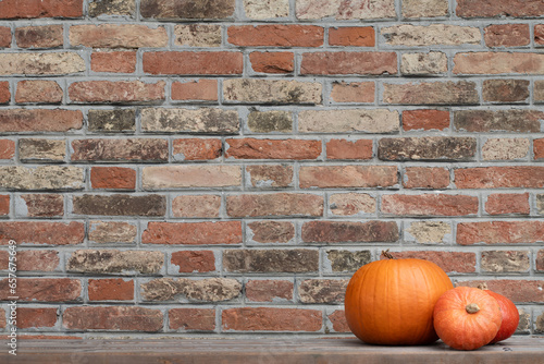 Background of a wall made of red fired bricks with three orange pumpkins lying on the side. There is a lot of space for text