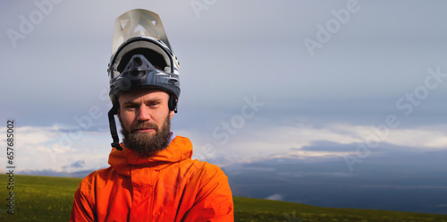 Portrait of a racer in full protection of a full face mask on a bicycle or motorcycle in the summer mountains. The concept of attracting youth to outdoor sports