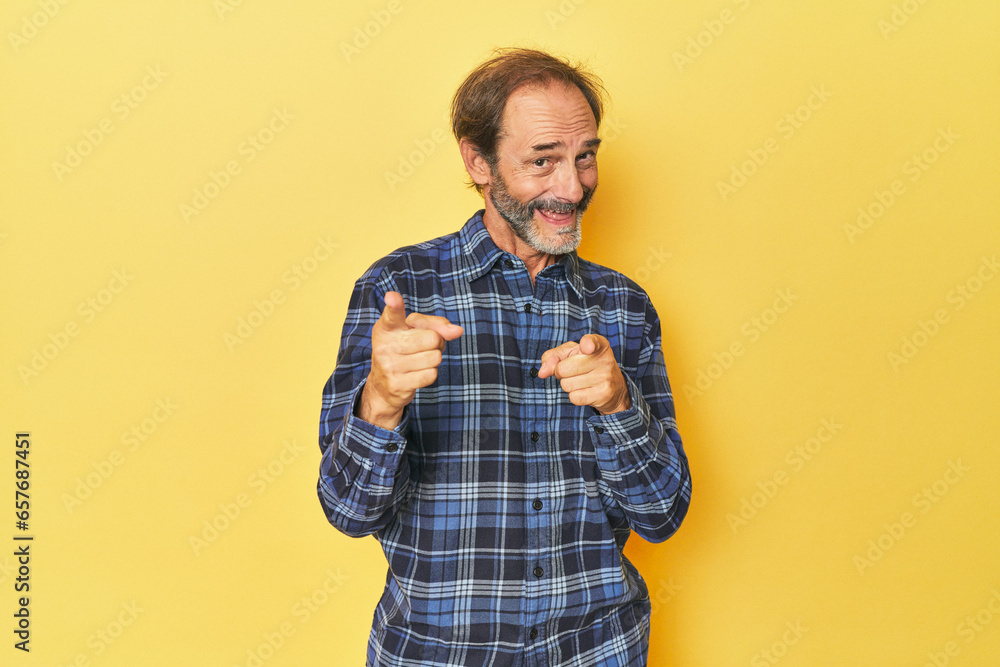 Caucasian middle-aged man in yellow studio pointing to front with fingers. Caucasian middle-aged man in yellow studio pointing to front with fingers.