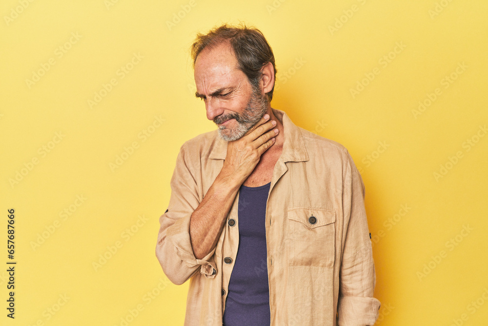 Caucasian middle-aged man in yellow studio suffers pain in throat due a virus or infection.