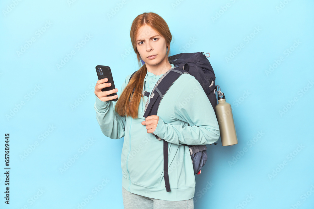 Redhead mountaineer with adventure backpack in blue studio Redhead mountaineer with adventure backpack in blue studio