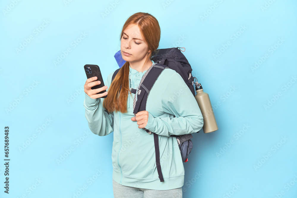 Redhead mountaineer with adventure backpack in blue studio Redhead mountaineer with adventure backpack in blue studio