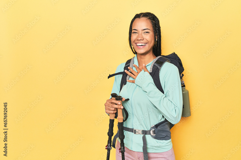 Indonesian woman with hiking gear on yellow laughs out loudly keeping hand on chest. Indonesian woman with hiking gear on yellow laughs out loudly keeping hand on chest.