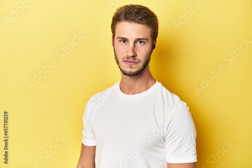 Young Caucasian man posing on a vibrant yellow studio backdrop