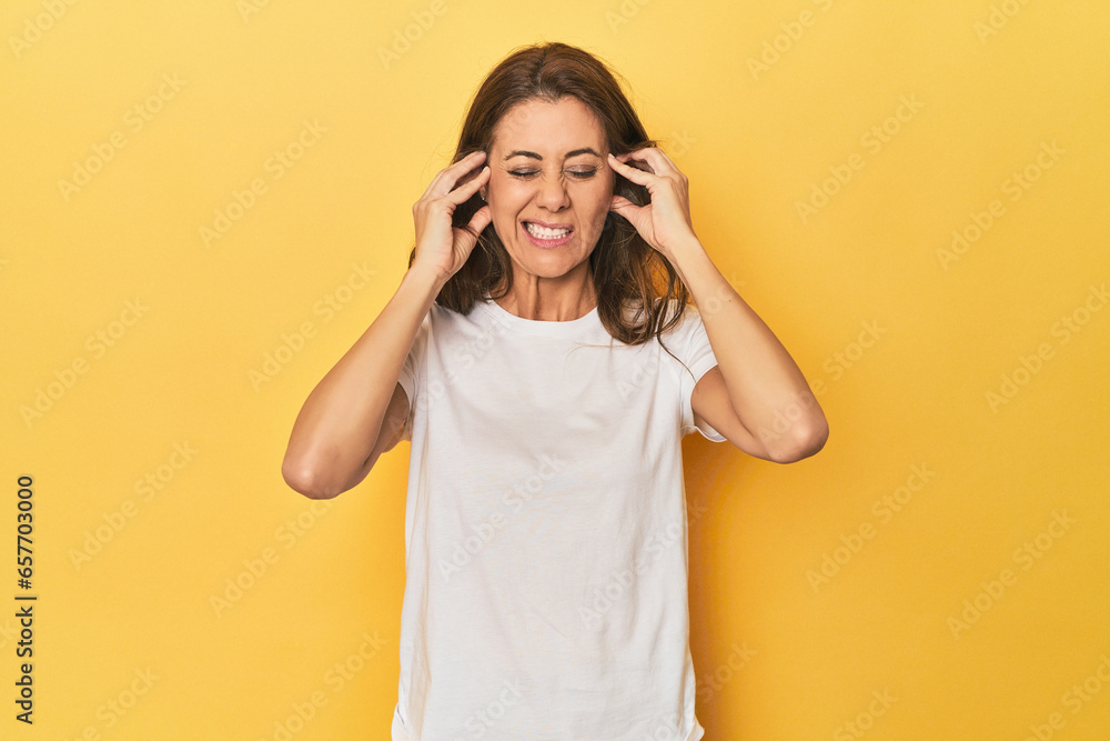 Middle-aged caucasian woman on yellow covering ears with hands. Middle-aged caucasian woman on yellow covering ears with hands.