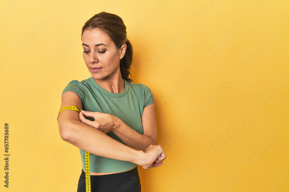 Middle aged woman measuring arm size on a yellow background Stock Photo