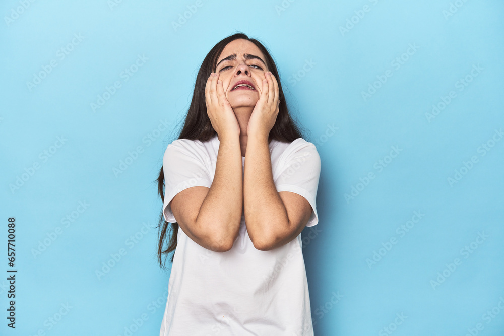 Young Caucasian woman on blue backdrop crying, unhappy with something, agony and confusion concept. Young Caucasian woman on blue backdrop crying, unhappy with something, agony and confusion concept.