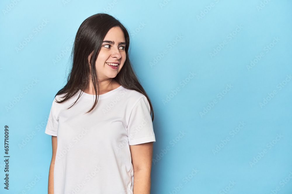 Young Caucasian woman on blue backdrop looks aside smiling, cheerful and pleasant. Young Caucasian woman on blue backdrop looks aside smiling, cheerful and pleasant.