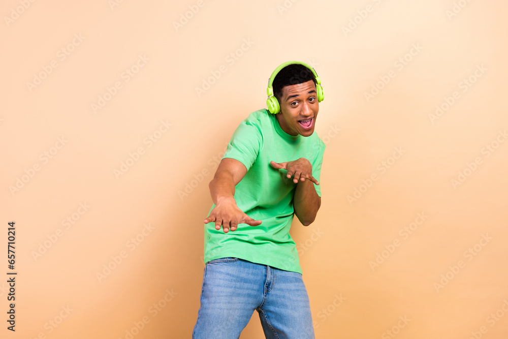 Photo portrait of nice young guy earphones dancing headphones dressed stylish green garment isolated on beige color background Photo portrait of nice young guy earphones dancing headphones dressed stylish green garment isolated on beige color background