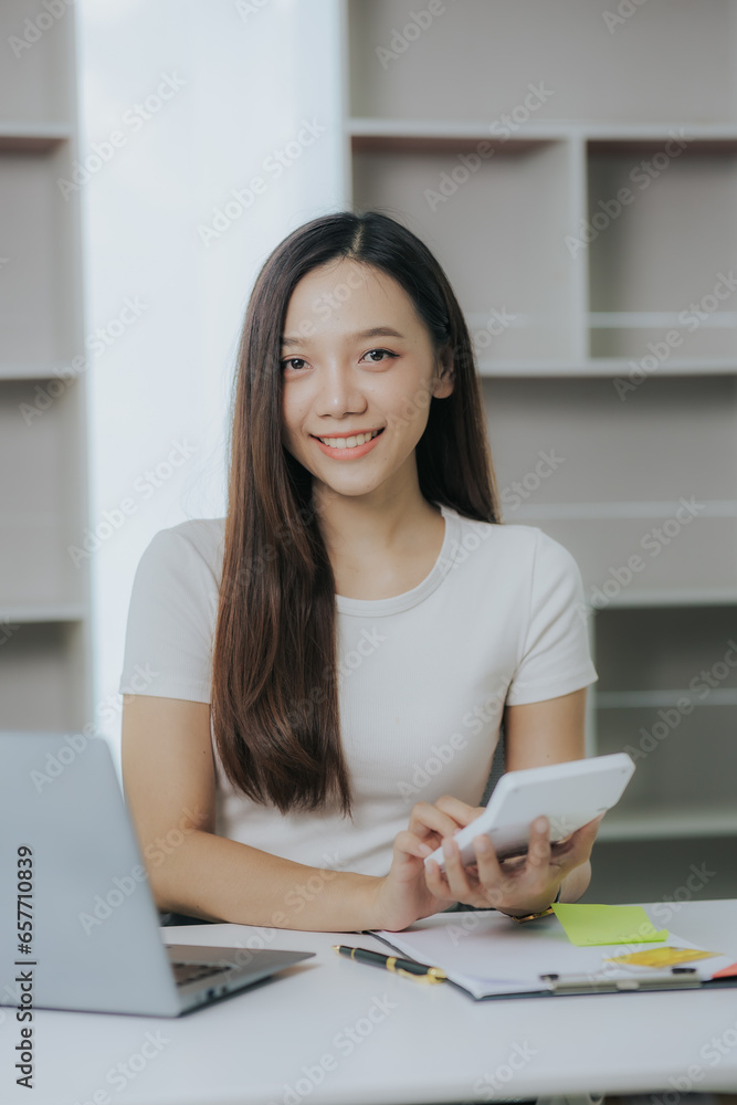 Happy Asian businesswoman paying online using mobile phone and laptop at office Happy Asian businesswoman paying online using mobile phone and laptop at office