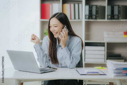 Portrait of an Asian businesswoman smiling happily working at a desk in the office. Businessman, freelance employee, online marketing, telemarketing concept.