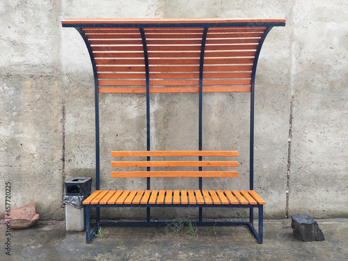 An unoccupied bus stop featuring a wooden and metal bench. A concept related to transportation on a rainy day following precipitation.