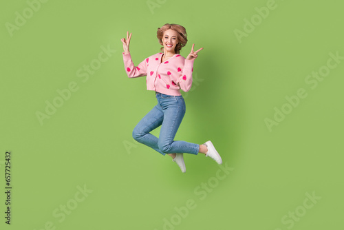 Full length photo of young jumping funky woman active showing double v-sign symbol peace wear pink shirt isolated on green color background