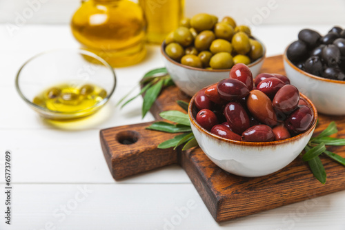 Green and black olives on a textured background. Different types of olives in bowls and olive oil with fresh olive leaves. Delicacy.Mediterranean Kitchen. Copy space.