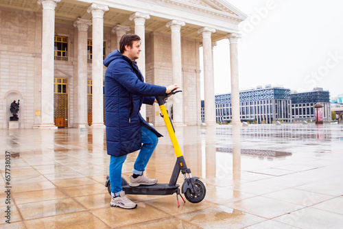 Male man and electric scooter in center of Astana. Electric scooter for rent, sharing. Electric transportation to move tourists around city. photo