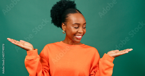 Tableau sur toile Beautiful young Black woman holds palms up weighing up choice, green studio