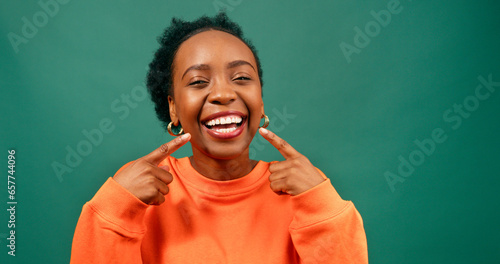 Beautiful young woman points to smile, white teeth, happy in green studio