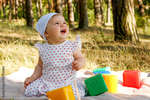 funny little girl in a scarf and dress in the summer in the park on a picnic with cubes